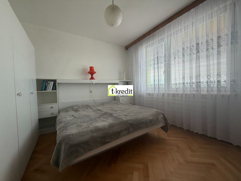 Bedroom in a 2-room apartment with wood-patterned flooring and large windows.
