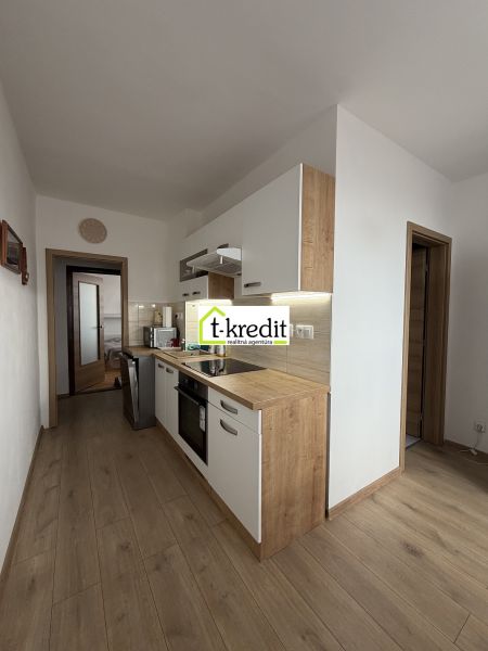 A kitchen in a 2-room apartment with a wooden decor floor and light cabinets.