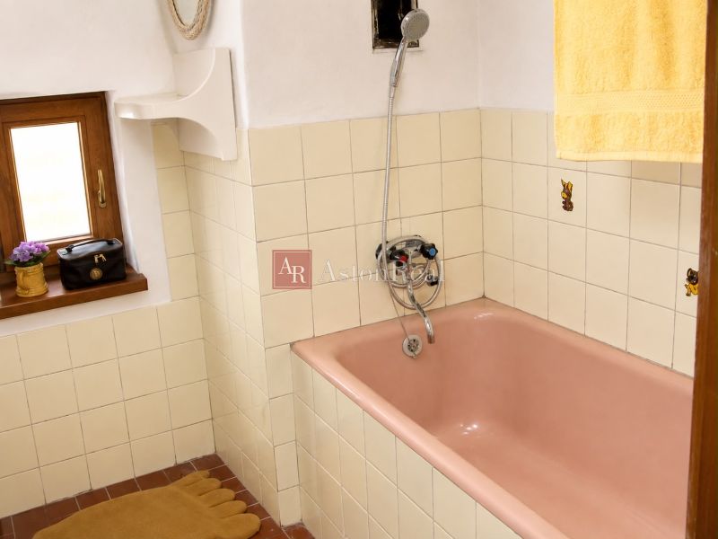 A bathroom in a cottage with a pink bathtub, beige tiles, and a small window.