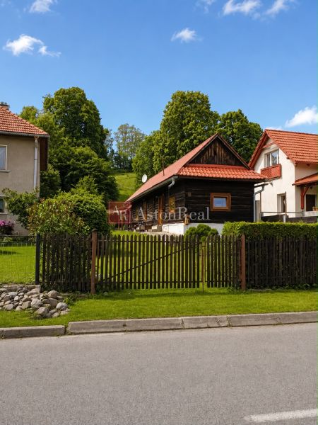 A cottage in Beňadiková surrounded by greenery, red roofs, wooden fence, paved road.