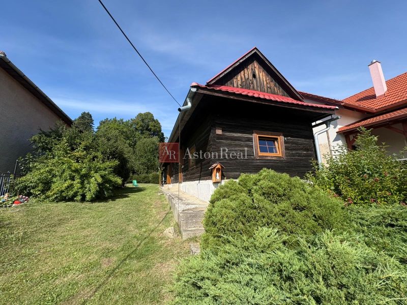 A wooden cottage in Beňadiková surrounded by greenery and shrubs on a sunny plot.