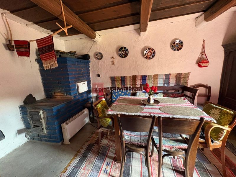 Rustic interior of a cottage with a blue stove, wooden ceiling, and decorated table.