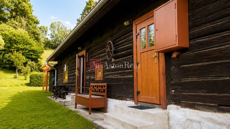 Wooden cottage in Beňadiková with wooden doors, a bench, and surrounding greenery.