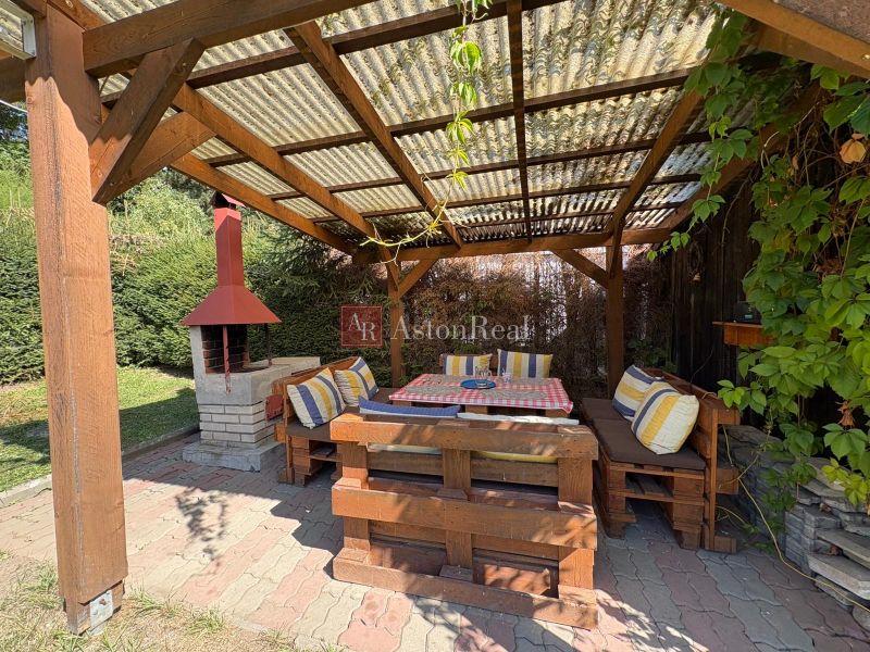 A cottage in Beňadiková with a covered terrace, outdoor seating, and a fireplace under a wooden pergola.