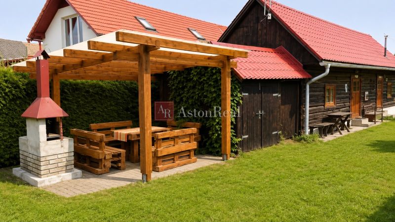 Wooden cottage in Beňadiková with garden seating and a grill on the green grass.