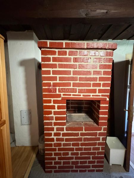 A brick fireplace in a cottage with a wooden ceiling and a floor with a wooden decor.