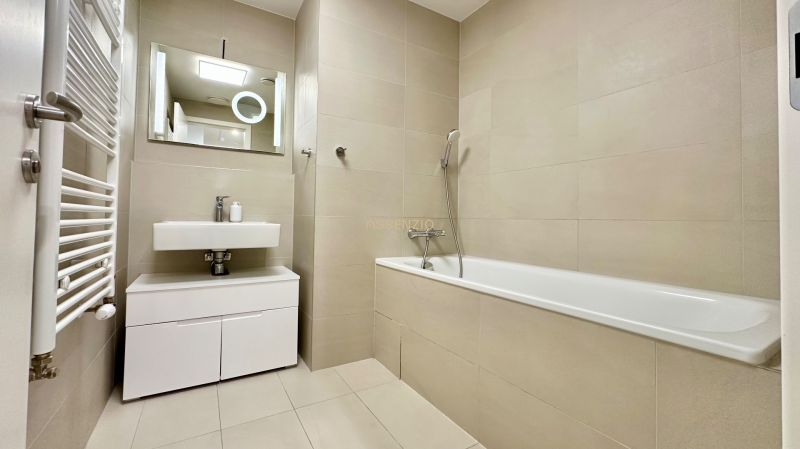 Bathroom in a 2-room apartment with a bathtub, sink, mirror, and ladder radiator.