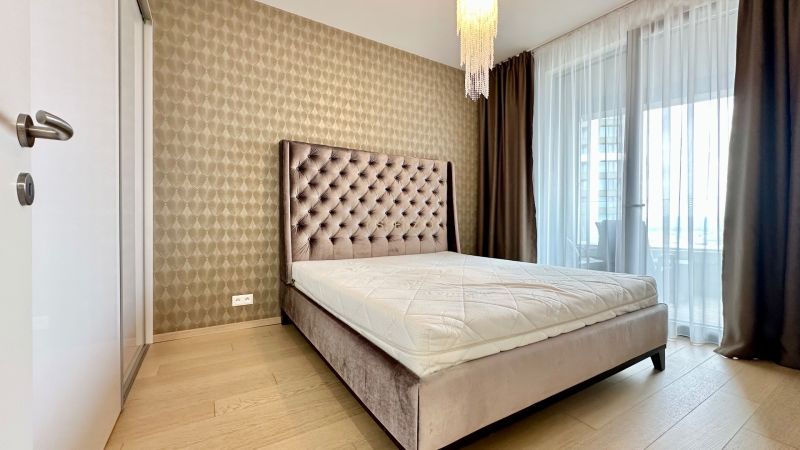 A bedroom with a bed, curtains, wallpaper, and a wooden decor floor in a 2-room apartment.