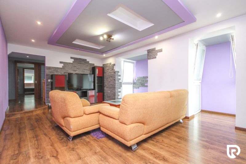 Living room with an orange sofa, television, and wooden decor flooring in a family house.