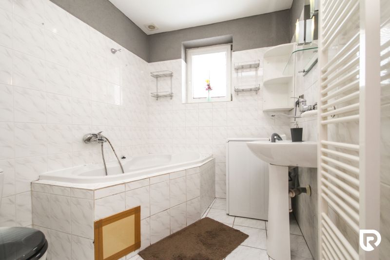 A bathroom in a family house with a bathtub, sink, and washing machine, tiled with white tiles.