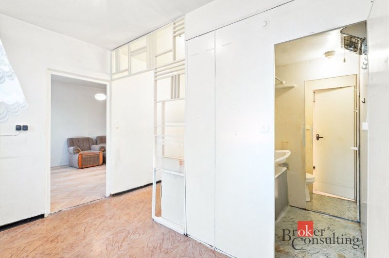 White interior of a 2-room apartment with wood-patterned flooring and a sofa in the background.