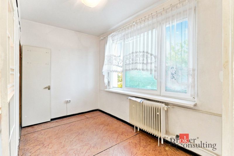 A room with a wooden decor floor, a radiator, and a large window in a 2-room apartment.