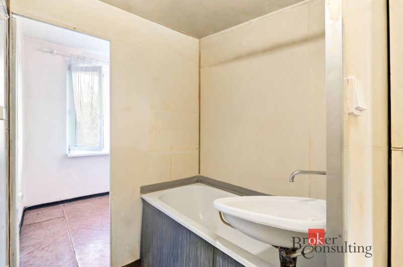 Bathroom with a bathtub and a sink in a 2-room apartment, without visible tiles.