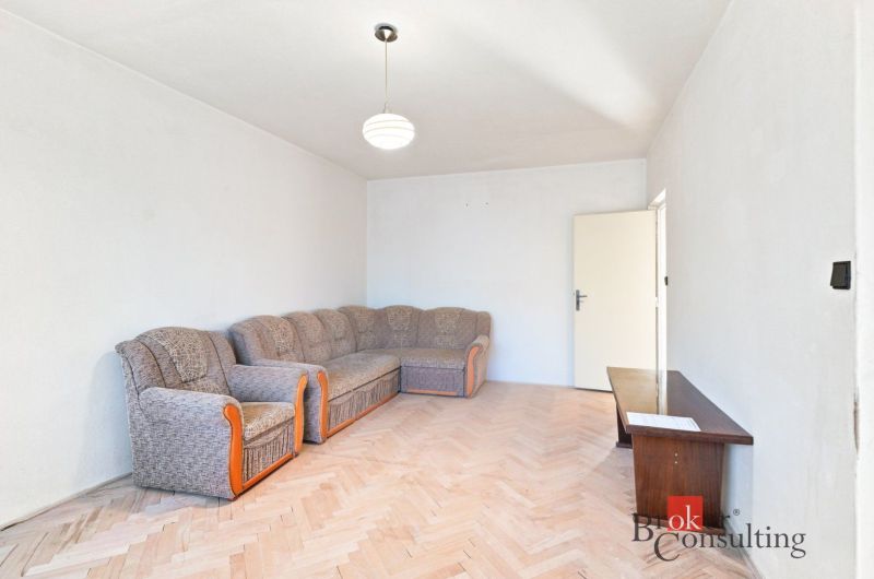 A living room in a two-room apartment with a wooden decor floor and a sofa.