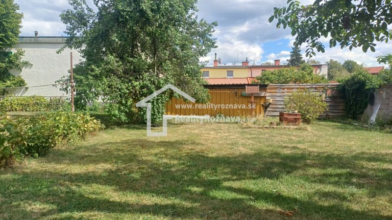 A garden of a family house in Rožňava with a lawn, trees, and a wooden gazebo.