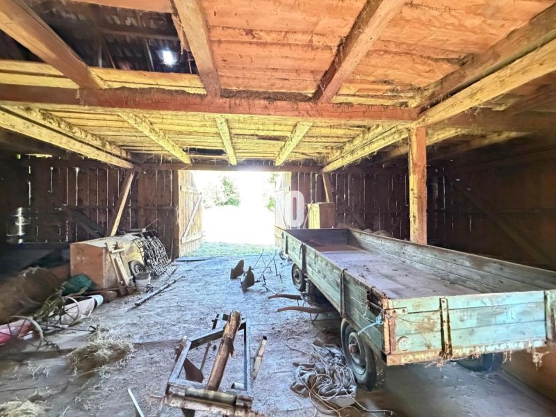 An interior view of a cabin with an old wooden structure, a trailer, and farming tools.