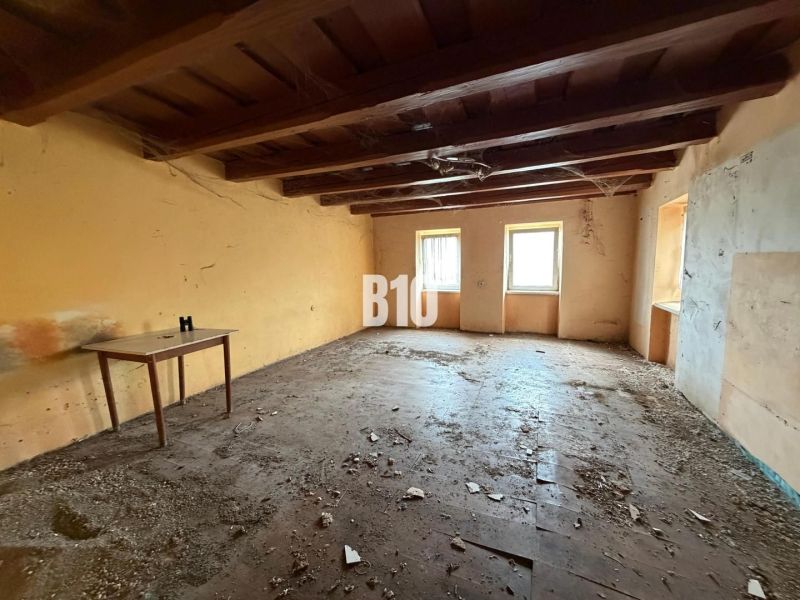 The interior of a family house with a wooden ceiling, an old table, and three windows.