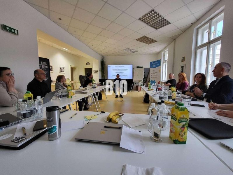 People in the office are discussing at a large table, with a presentation and refreshments.