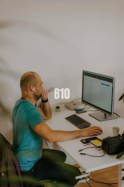 A man is working on a computer in an office, surrounded by technology and notes.