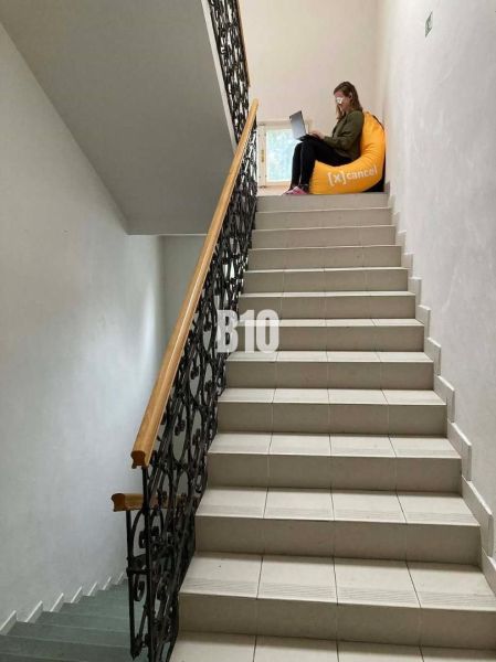 A person with a laptop is sitting on a yellow bean bag on the office stairs.