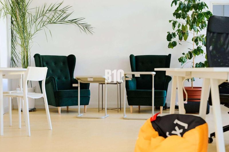 Offices with dark green chairs, white desks, and plants on a floor with wooden decor.