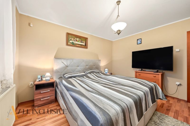 Bedroom in a family house with a bed, television, and wooden decor flooring.