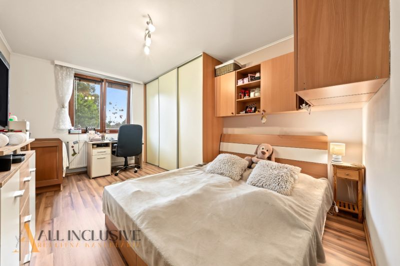 A bedroom in a family house with a bed, a desk, and a wooden decor floor.