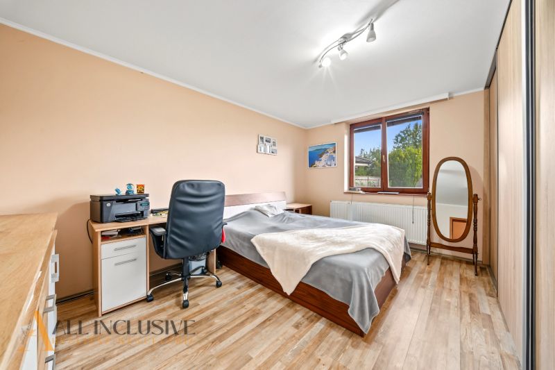 Bedroom in a family house with a bed, a desk, and a mirror, floor with wooden decor.