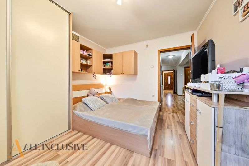 A bedroom in a family house with a wooden decor floor, a large bed, and a wardrobe.