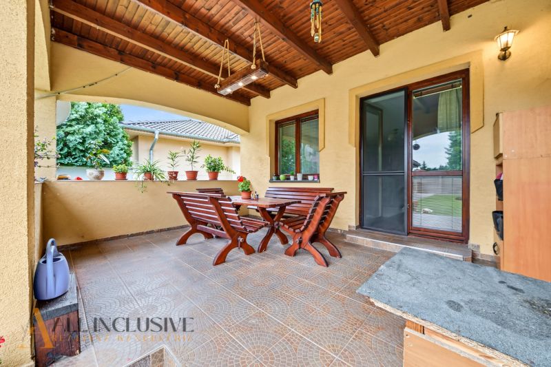 Covered terrace of a family house with wooden seating and flowers on the windowsill.