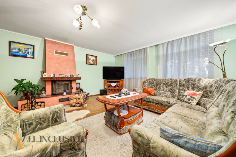 Living room in a family house with a fireplace, floral sofa set, and wooden decor flooring.