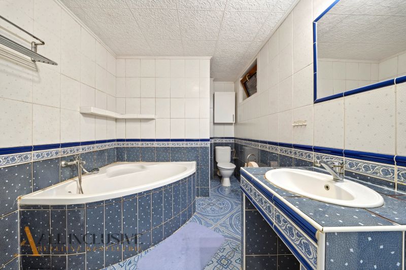 Bathroom in a family house with a corner bathtub, sink, toilet, and blue tiles.