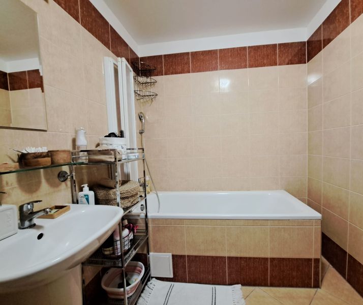 A bathroom with a bathtub and a sink in a 2-room apartment with tiled flooring.