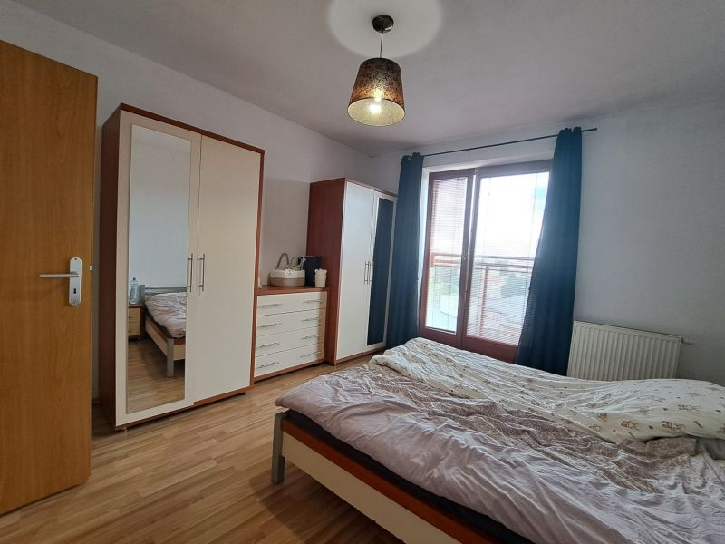 Bedroom in a 2-room apartment with wood-patterned flooring, a wardrobe, and a large window.