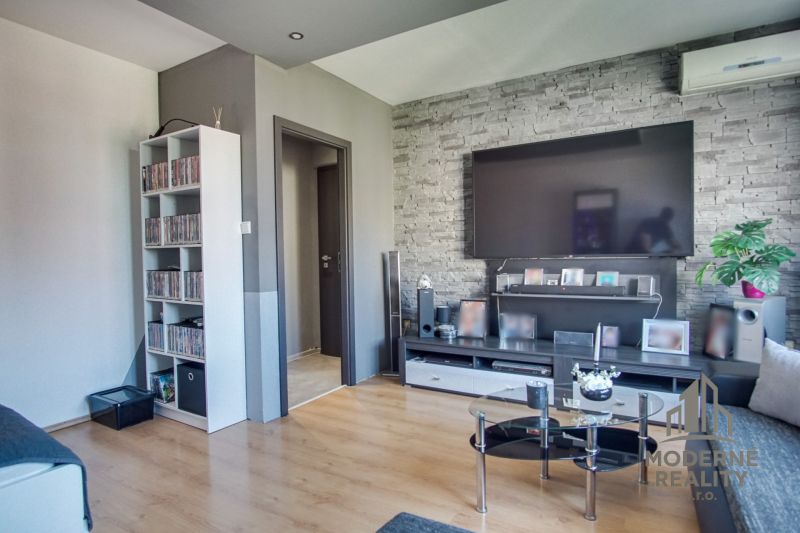 Living room in a 3-room apartment with a TV, brick cladding, and a wooden decor floor.
