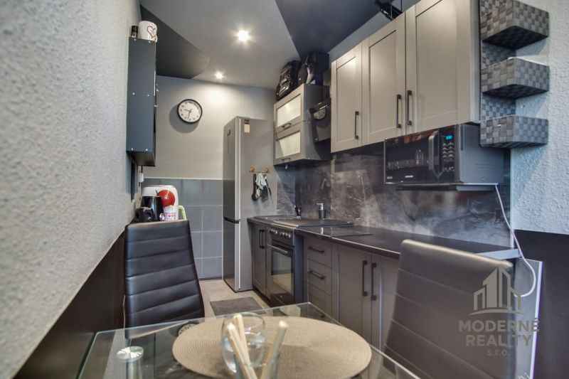A kitchen in a 3-room apartment with dark gray kitchen cabinets and a dining table with a glass top.