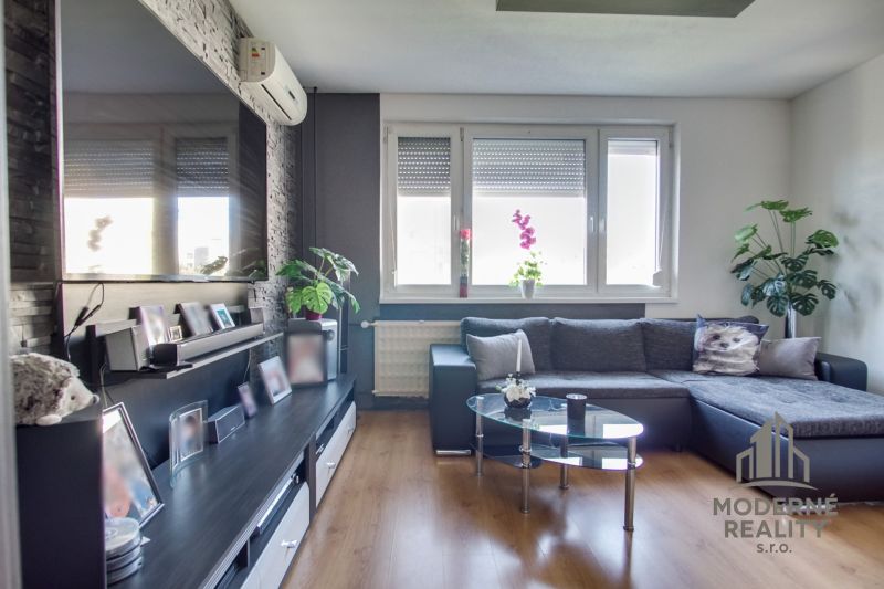 Living room in a 3-room apartment with a wooden decor floor, a sofa, and a large television.