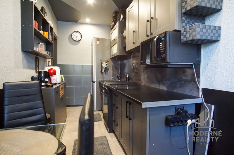 A stylish kitchen in a 3-room apartment with dark furniture and appliances.