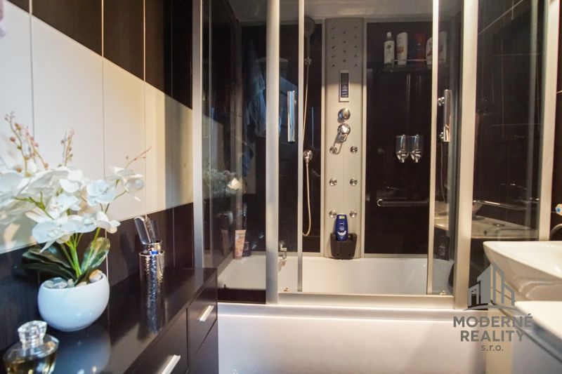 A bathroom in a 3-room apartment with a bathtub and a shower box, complemented by artificial flowers.