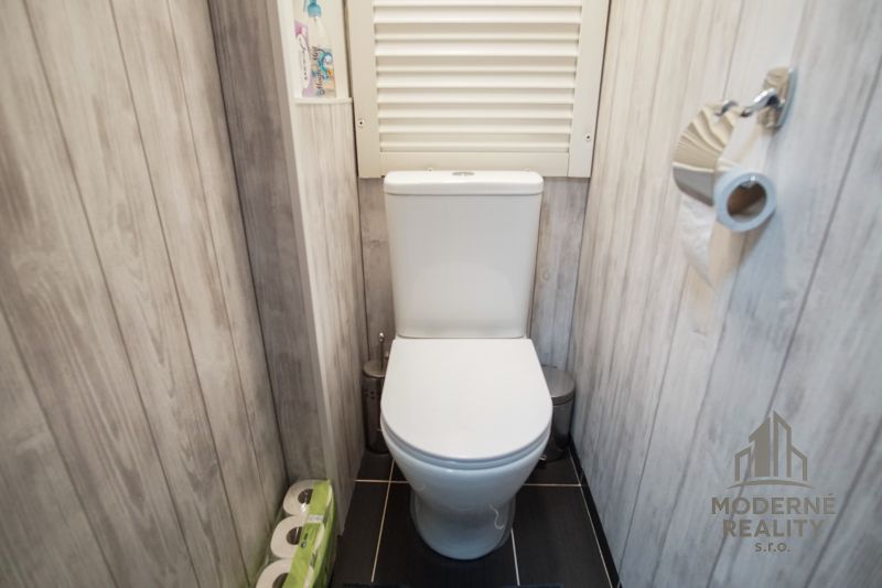 A toilet in a 3-room apartment with wood decor on the walls and a black floor.