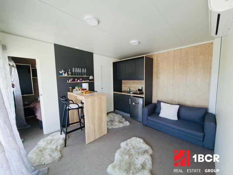 Recreational apartment with a kitchenette, dining table, and sofa, floor with wooden decor.