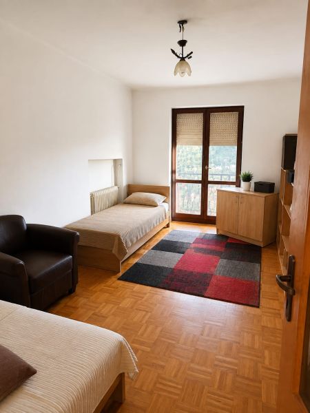 A room in a 3-room apartment with beds, a chair, a carpet, and a floor with a wooden decor.