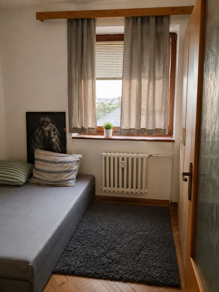 A room in a 3-room apartment with a bed, curtains, and a carpet on a floor with a wooden decor.