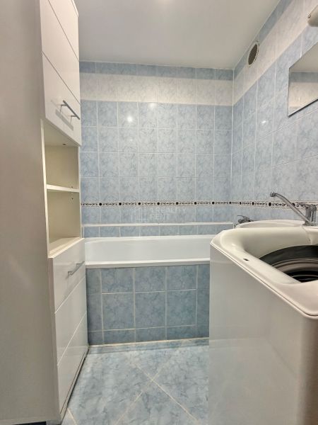 A bathroom with light blue tiles, a bathtub, and a white sink in a 3-room apartment.