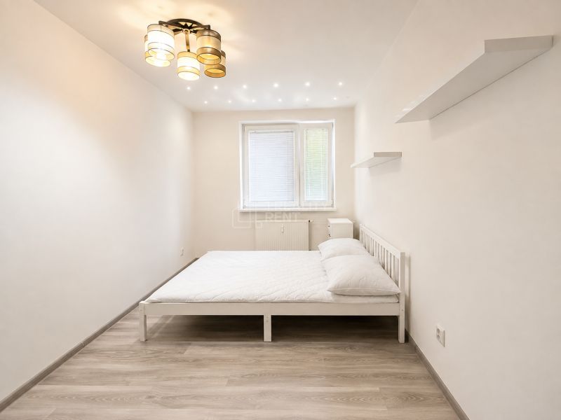 A bedroom with a white bed and a wooden decor floor in a 3-room apartment.