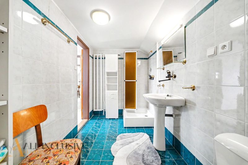 A bathroom in a family house with blue tiles, a shower, and a stylish mirror.