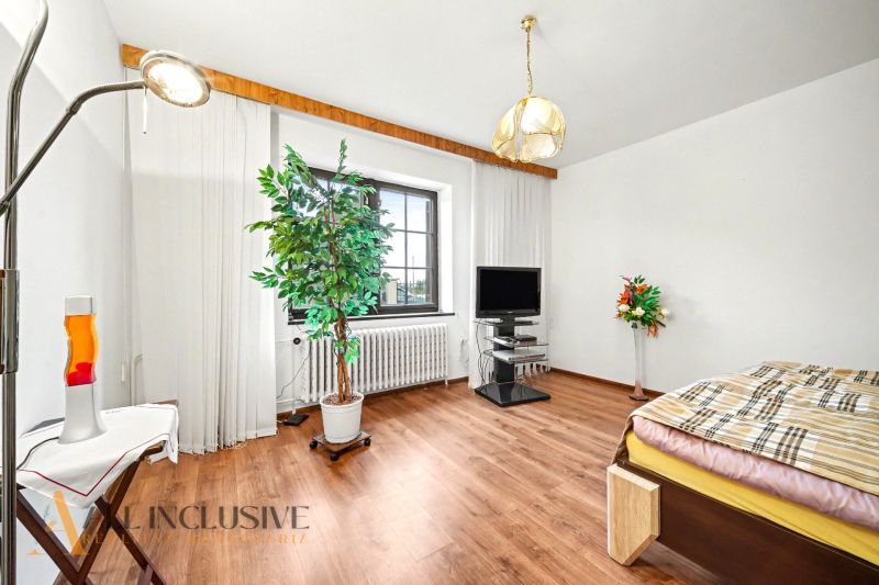 A room in a family house with a wooden decor floor, a television, plants, and a bed.