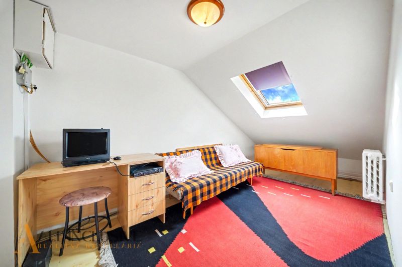 Attic room in a family house with a desk, sofa, and colorful carpet.