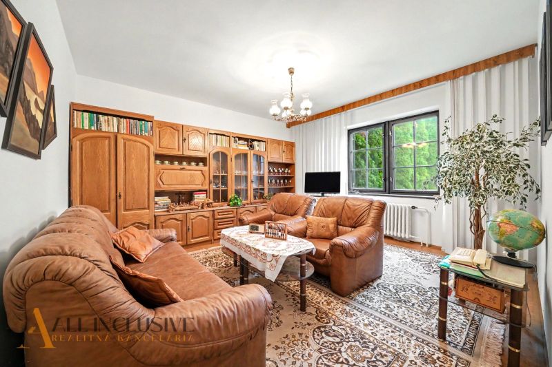 Living room in a family house with a leather sofa, shelving unit, and a window overlooking the green exterior.