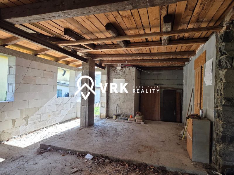 The interior of a family house with a wooden beam ceiling and an unfinished floor.